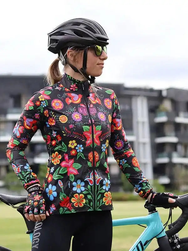 Woman in vibrant floral cycling jersey and helmet, standing with road bike outdoors