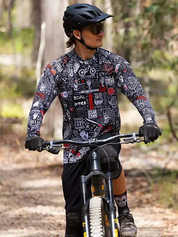 Man riding mountain bike in forest wearing graphic long-sleeve cycling jersey and helmet
