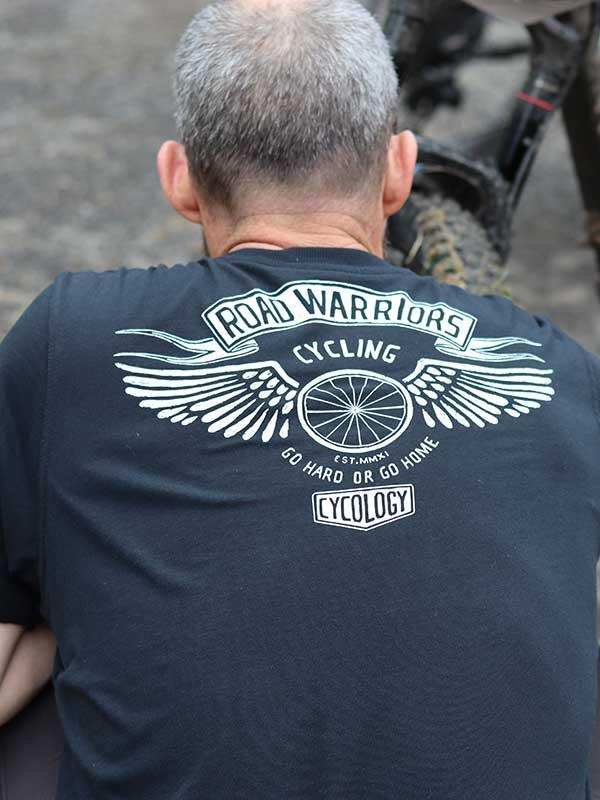 Man wearing black cycling t-shirt with 'Road Warriors Cycling' graphic and winged wheel design