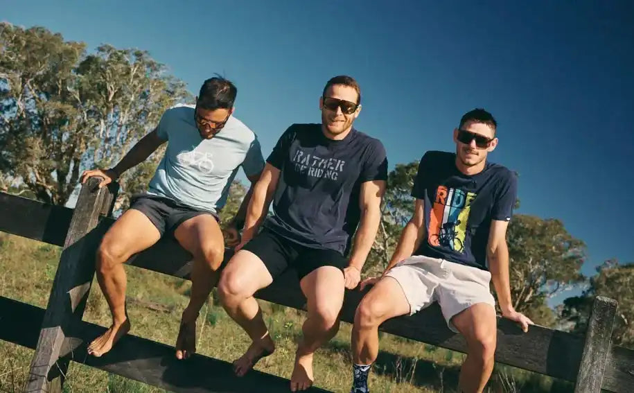 Men in cycling apparel relaxing on a fence outdoors under clear blue skies