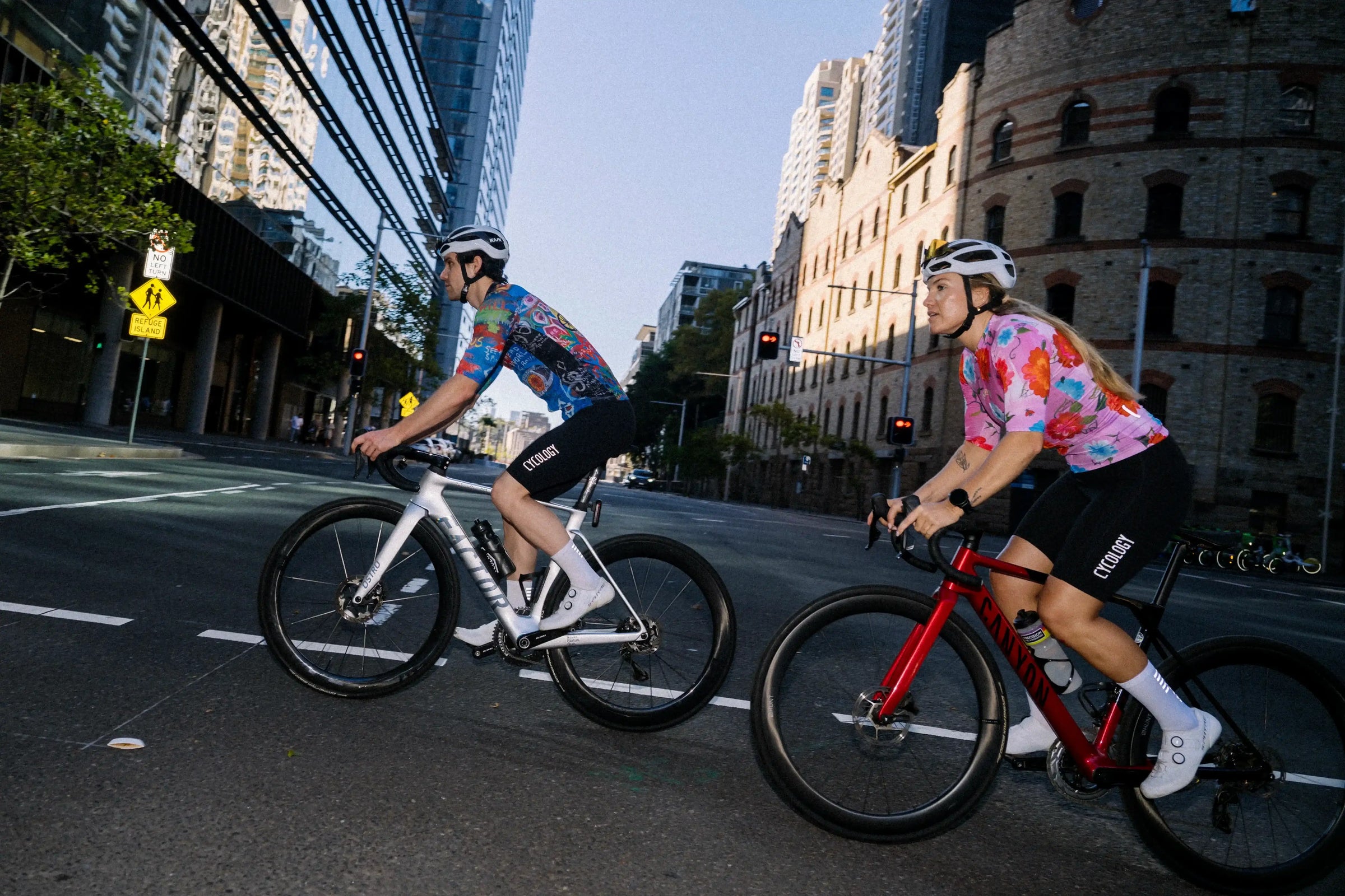 Man and woman cycling in colorful jerseys on city streets, wearing helmets and performance gear