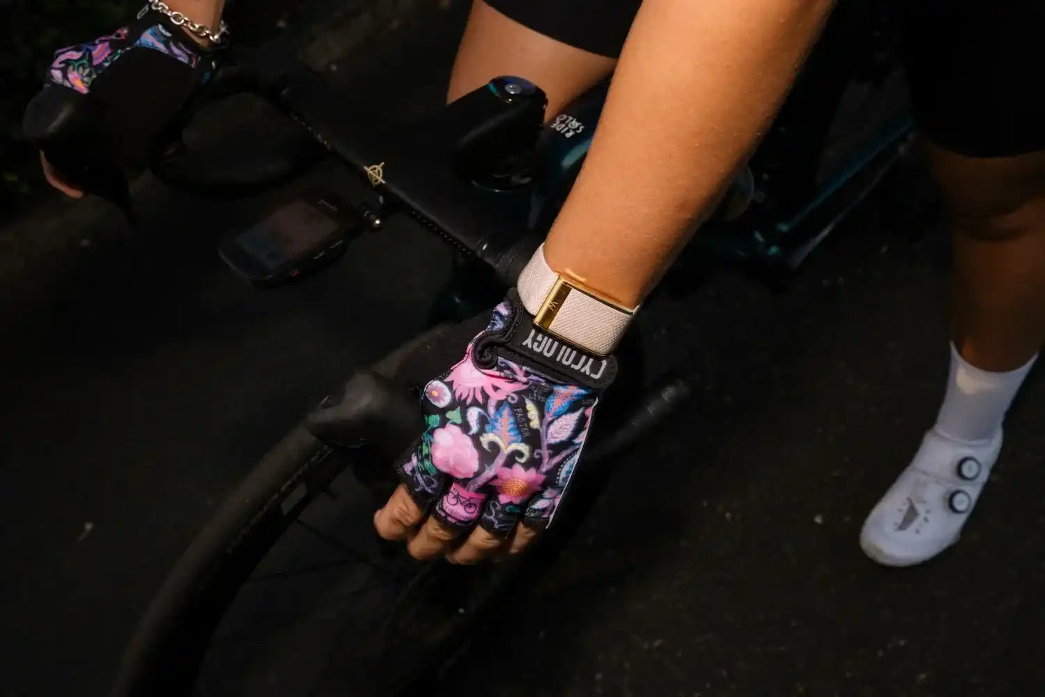 Cycling gloves with floral pattern, worn on bike handlebars, featuring breathable fabric and wrist strap for comfort.