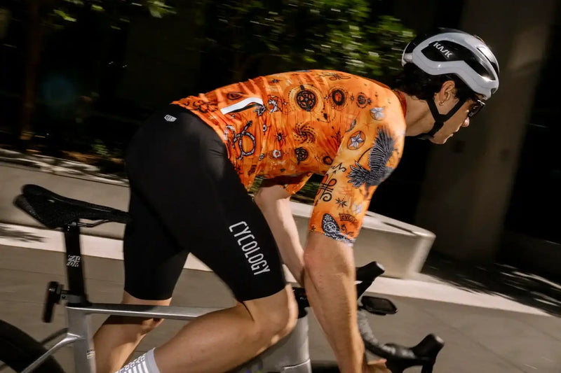 Cyclist in orange patterned jersey and black Cycology shorts riding road bike at night