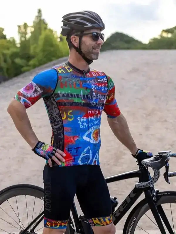 Man in colorful cycling jersey and shorts, standing with road bike outdoors