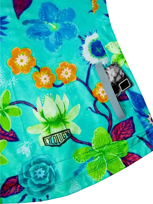 Vibrant floral cycling shorts with bold blue, orange, green blooms on teal fabric, featuring reflective strip and brand tag.