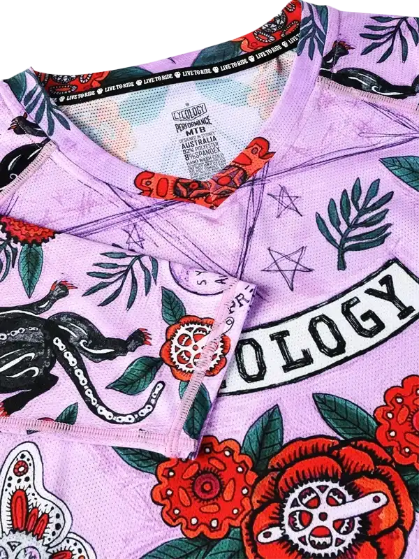 Purple cycling jersey with floral, tattoo-style print and 'OLOGY' text, featuring performance fabric and bold design details