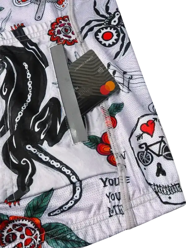 White cycling shorts with bold tattoo-style graphics, skulls, roses, and bike motifs on breathable fabric