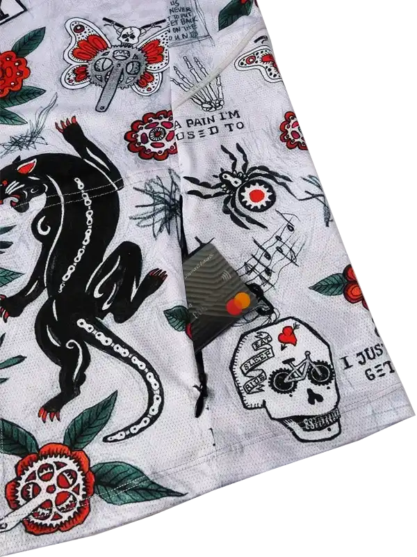 Men's cycling shorts with bold tattoo-style graphics including skulls, panthers, and roses on white fabric