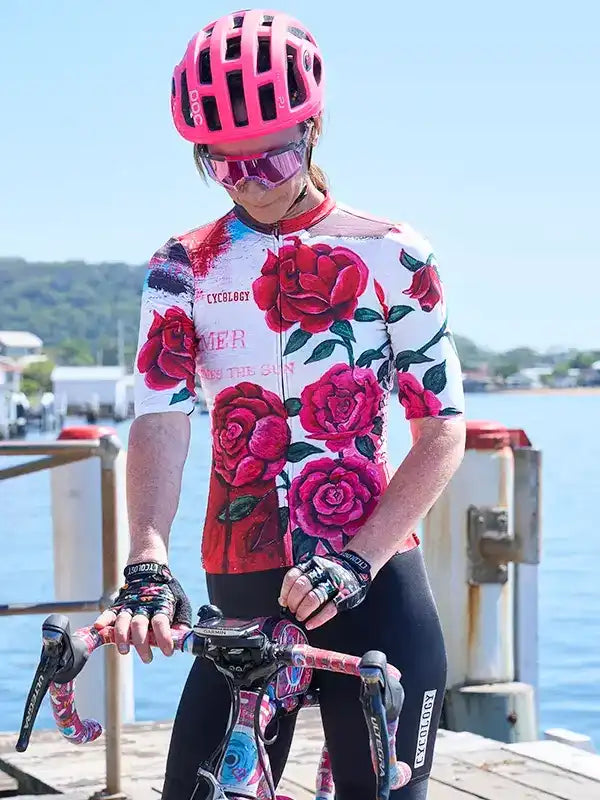 Woman in floral cycling jersey and pink helmet on dock by water, ready to ride