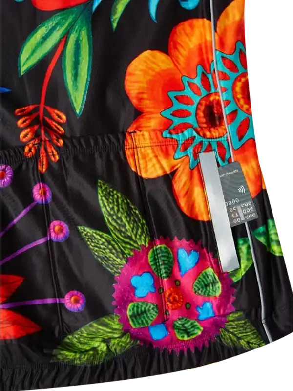 Vibrant floral cycling jersey with bold orange, pink, and green blooms on black fabric, featuring rear pockets and tag detail.