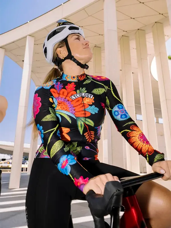 Woman in vibrant floral cycling jersey and helmet, riding bike under modern architecture