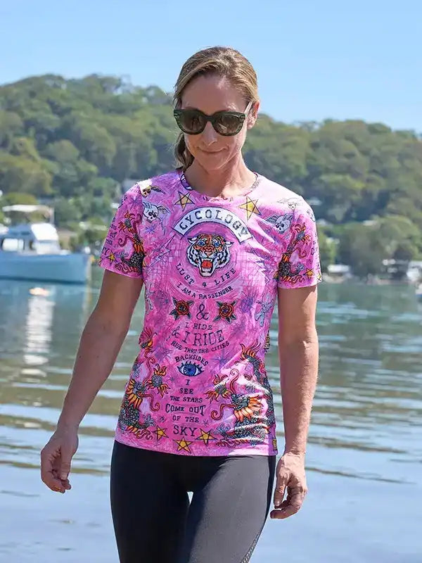 Woman wearing pink cycling jersey with tiger graphic, sunglasses, by water