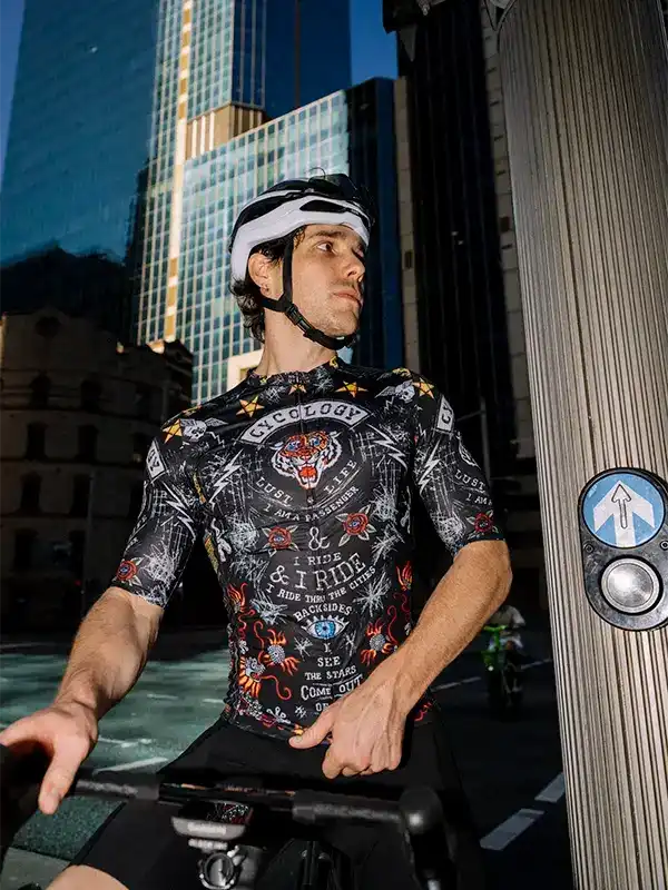 Man wearing graphic cycling jersey with tiger design, riding in urban cityscape