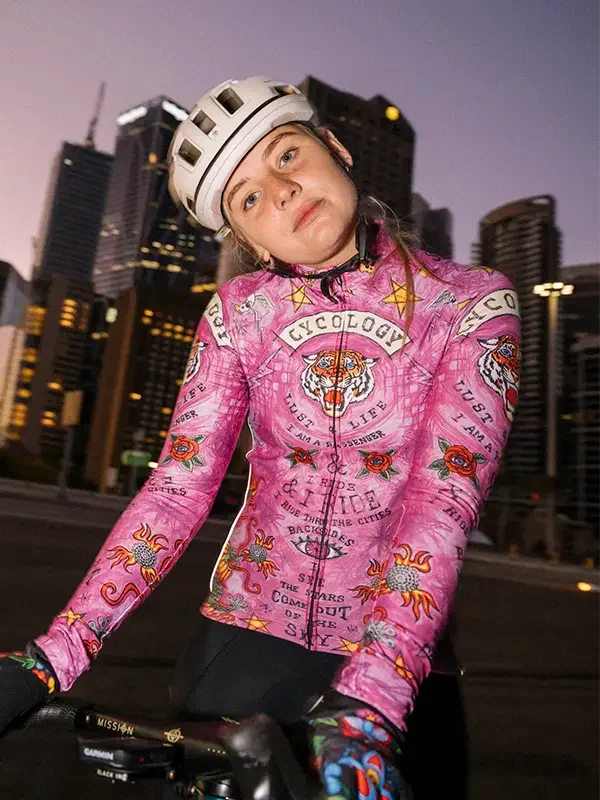 Woman in pink tattoo-style cycling jersey with tiger graphic, riding bike in city at dusk
