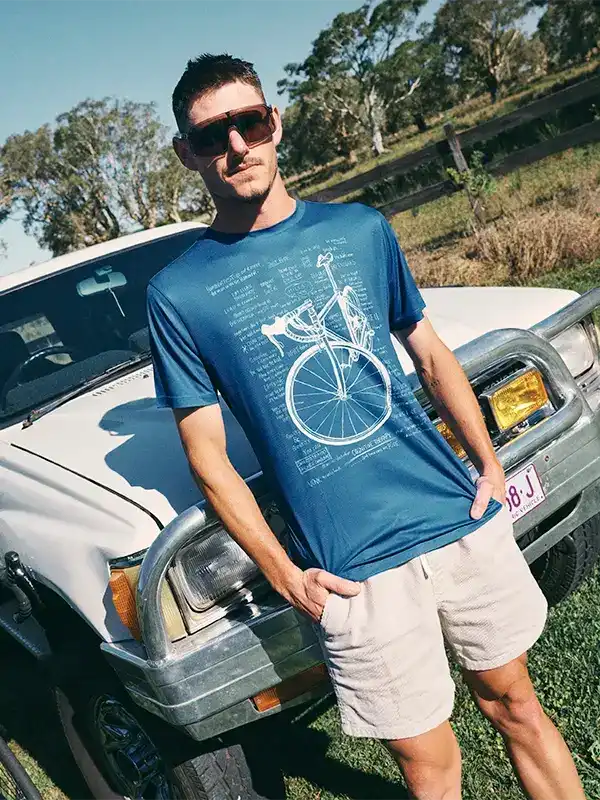 Man wearing blue cycling graphic tee with vintage bike print, standing by white truck outdoors