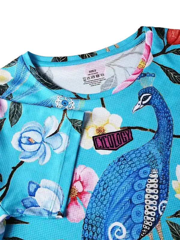 Blue cycling jersey with peacock and floral print, featuring breathable fabric and brand patch detail.