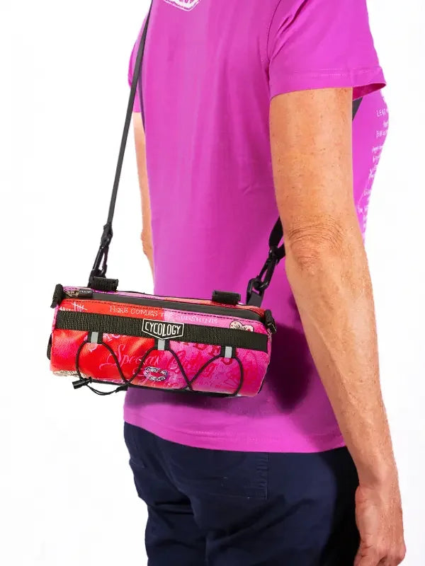 Cycology pink cycling bag with black straps worn crossbody by cyclist in magenta jersey