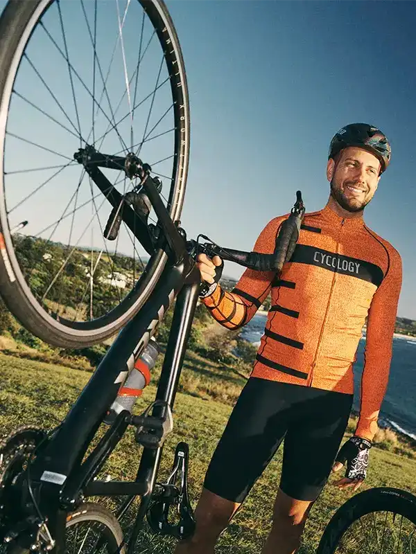 Man in orange cycling jersey and black shorts holding bike, outdoor ride gear