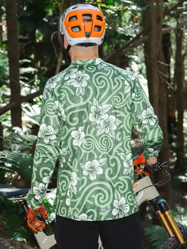 Men's green floral cycling jersey with white hibiscus print, worn with helmet in forest trail setting