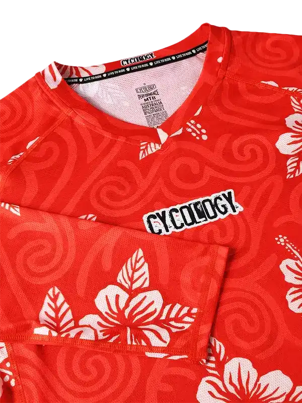 Red cycling jersey with white hibiscus flowers and swirl pattern, featuring CYCOLOGY logo and performance fabric tag