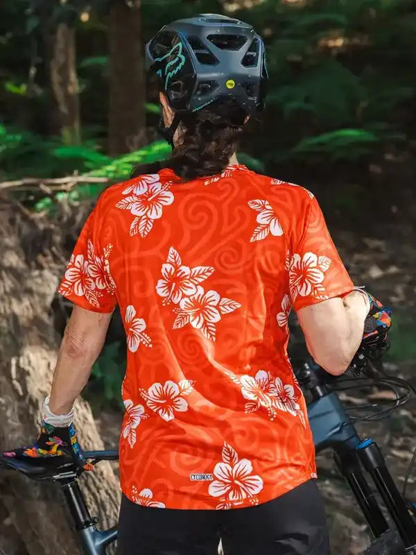 Woman in orange floral cycling jersey and helmet on forest trail, mountain biking gear