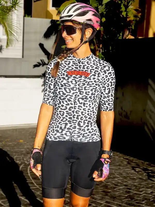 Woman in leopard print cycling jersey and black bib shorts, wearing pink helmet and sunglasses