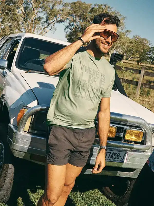Man in olive cycling tee and shorts leaning on white truck outdoors