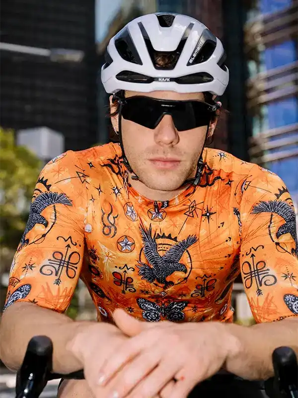 Man cycling in vibrant orange jersey with eagle print, wearing helmet and sunglasses