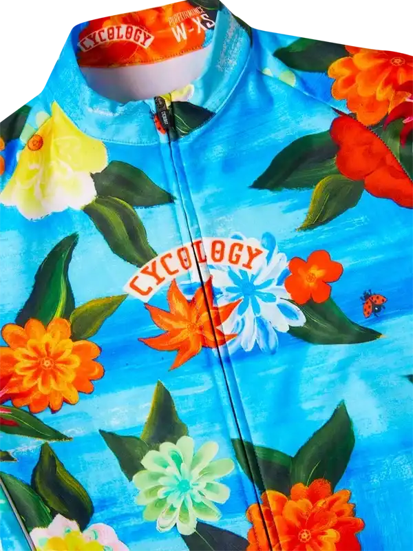 Vibrant floral cycling jersey with bold orange, yellow, and blue flowers on a bright blue background, featuring a full zipper and brand logo.