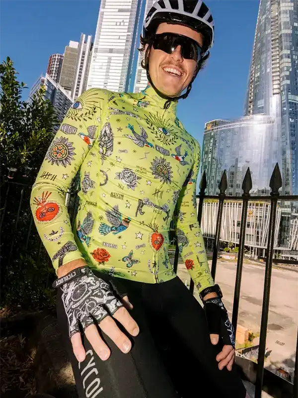 Man in vibrant green cycling jersey with tattoo-style graphics, helmet, and gloves, urban skyline background