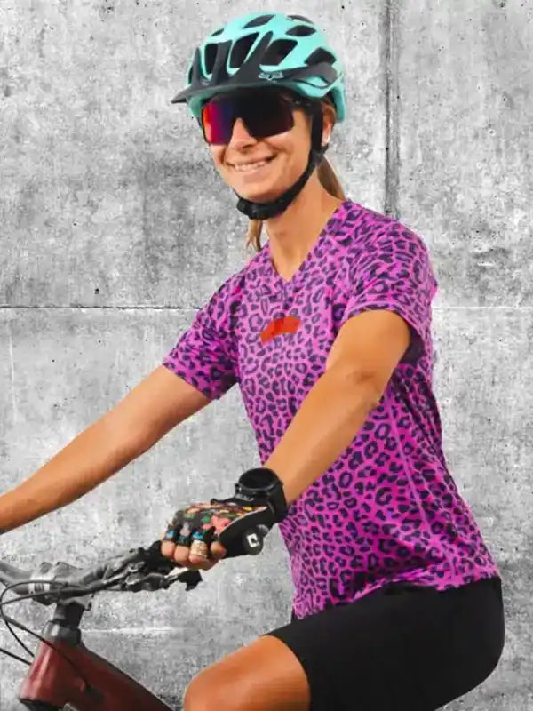 Woman cycling in vibrant purple leopard print jersey, helmet, and sunglasses