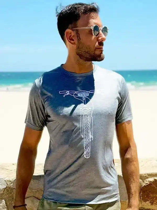 Man wearing gray cycling t-shirt with bike graphic, beach background, stylish men's cycling apparel