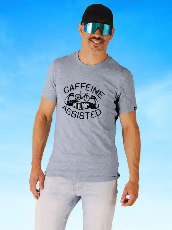 Man wearing gray 'Caffeine Assisted' cycling t-shirt with bike graphic, sunglasses, and cap against blue sky