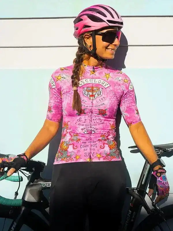 Woman in pink cycling jersey with tiger graphic, helmet, and gloves, standing with road bike