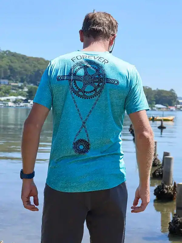 Man wearing blue cycling shirt with 'FOREVER' and gear design, standing by waterfront