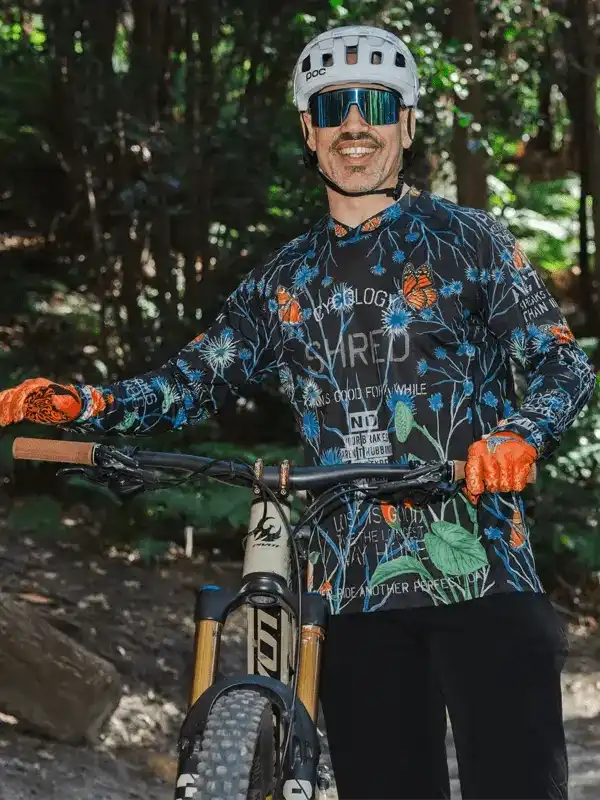 Man in floral cycling jersey and helmet on mountain bike trail, wearing sunglasses and gloves