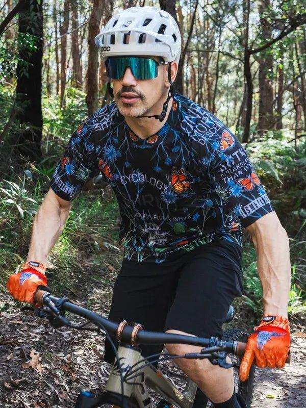 Man mountain biking in forest wearing floral cycling jersey, helmet, and orange gloves