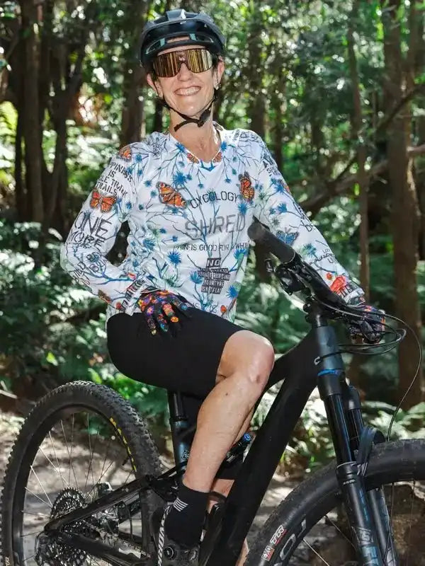 Woman in floral cycling jersey and helmet riding mountain bike on forest trail