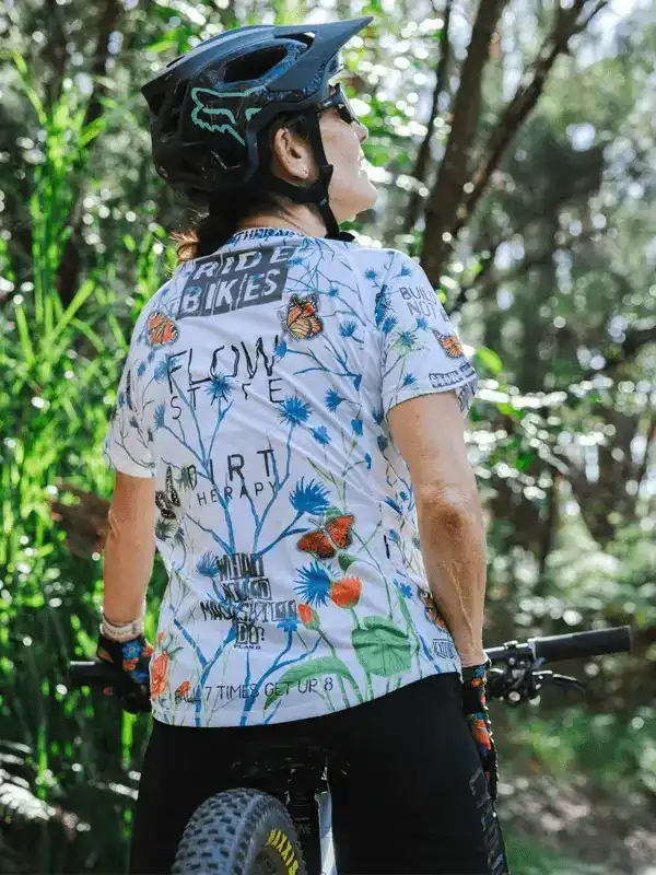 Woman in floral cycling jersey and helmet riding mountain bike through forest trail