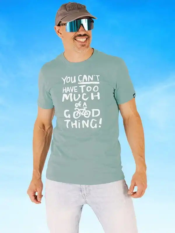 Man wearing cycling-themed t-shirt with 'You can't have too much of a good thing!' slogan, sunglasses, and cap against blue sky
