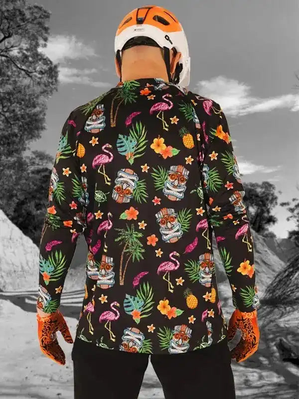 Men's tropical print cycling jersey with flamingos, pineapples, and tiki masks, worn with helmet and gloves