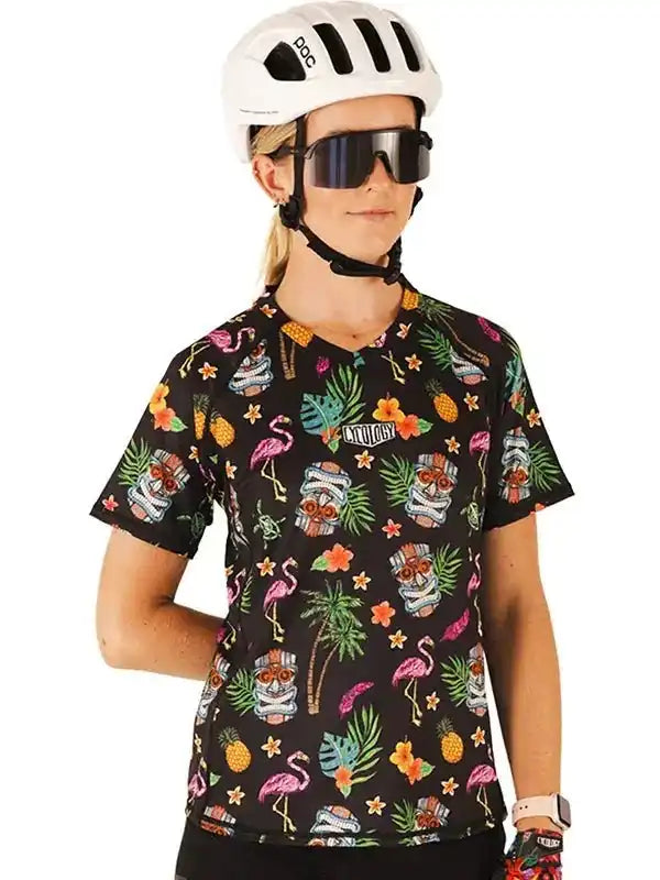 Woman wearing tropical print cycling jersey with flamingos, pineapples, and tiki masks, paired with POC helmet and sunglasses