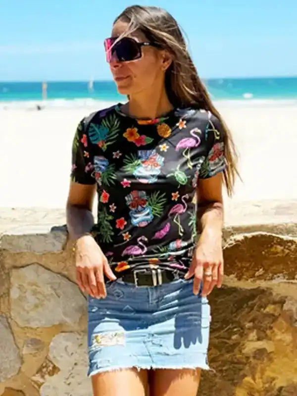 Woman wearing tropical print t-shirt with flamingos and flowers, denim skirt, beach background