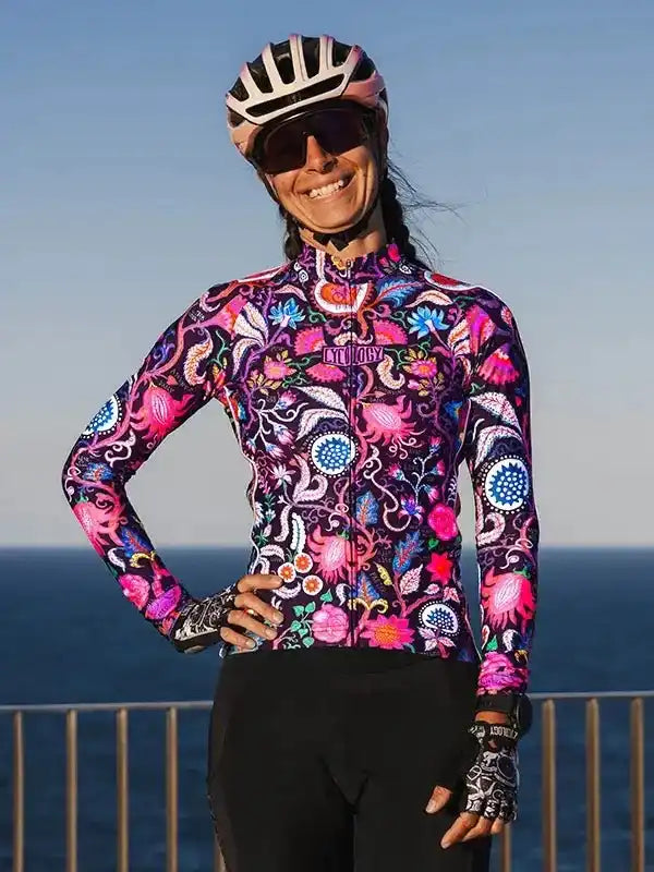 Woman in vibrant floral cycling jersey and helmet by the sea, wearing sunglasses and gloves