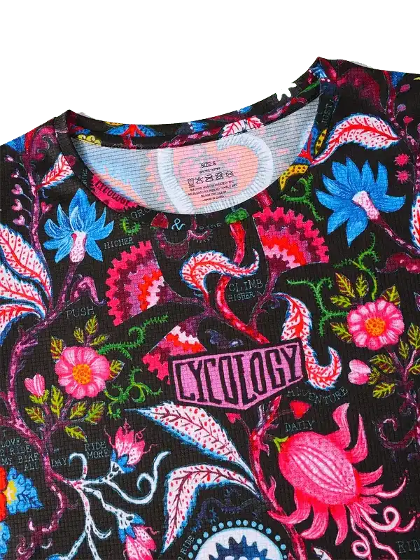 Vibrant floral cycling jersey with bold pink, blue, and red patterns on black fabric, featuring 'CYCOLOGY' logo.