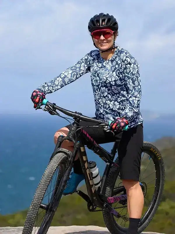 Woman in floral cycling jersey and helmet on mountain bike overlooking ocean, ready for trail ride