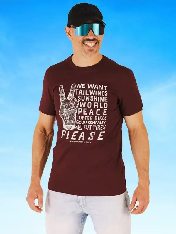 Man wearing cycling-themed graphic tee with peace sign, sunglasses, and cap against blue sky