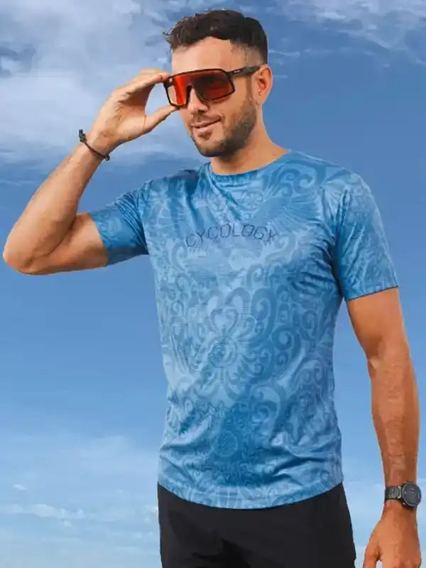 Man wearing blue patterned cycling jersey with 'CYCOLOGY' logo, sunglasses, against sky background