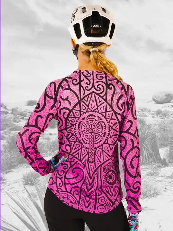 Woman wearing pink patterned long-sleeve cycling jersey with black geometric design, white helmet, outdoors