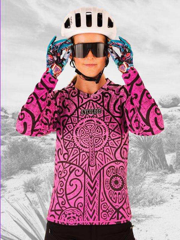 Woman in pink patterned cycling jersey, helmet, and gloves adjusting sunglasses outdoors
